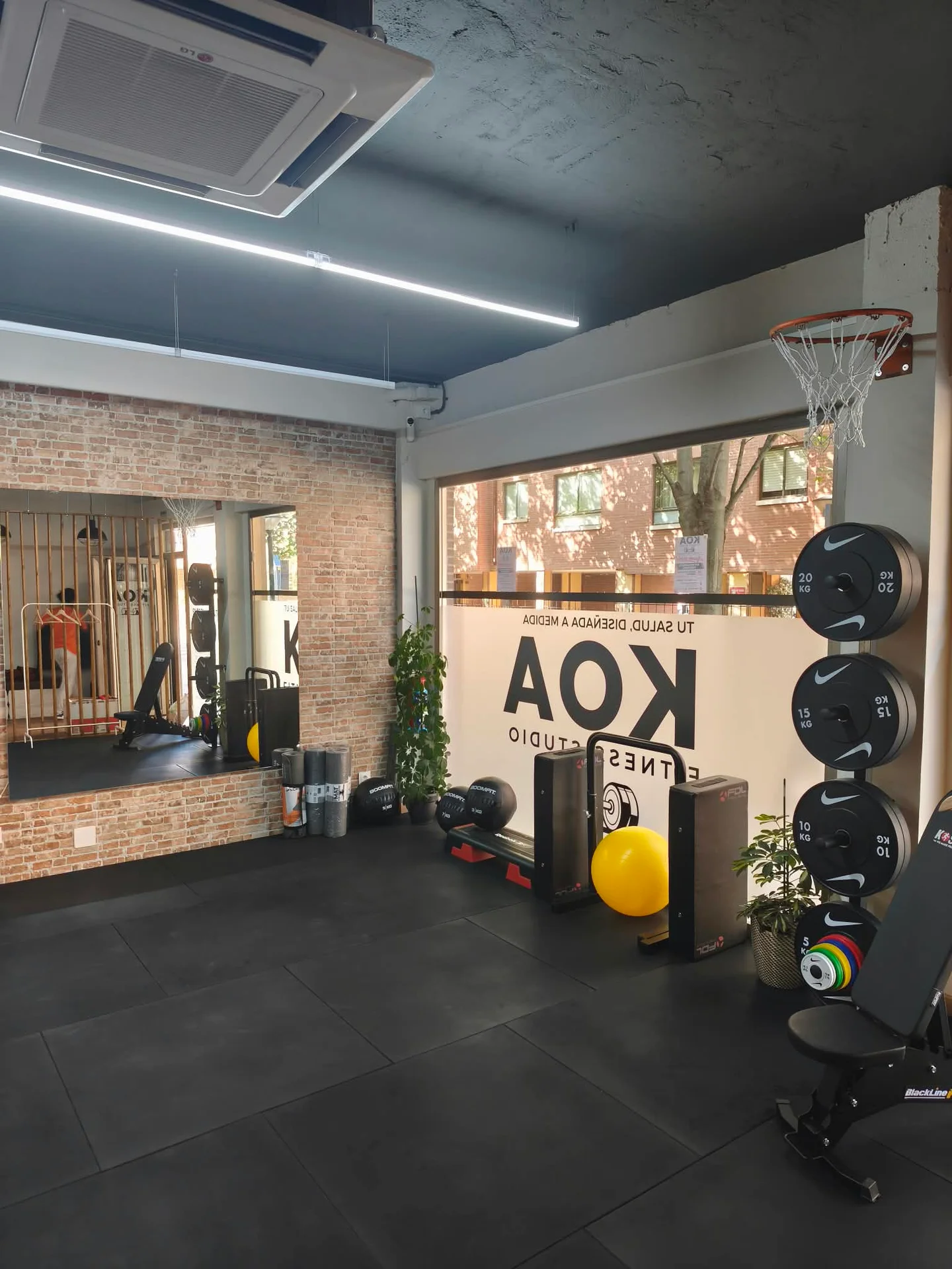 Interior de Koa Fitness Studio: ventanal con luz natural, espejo sobre pared de ladrillo y material de entrenamiento